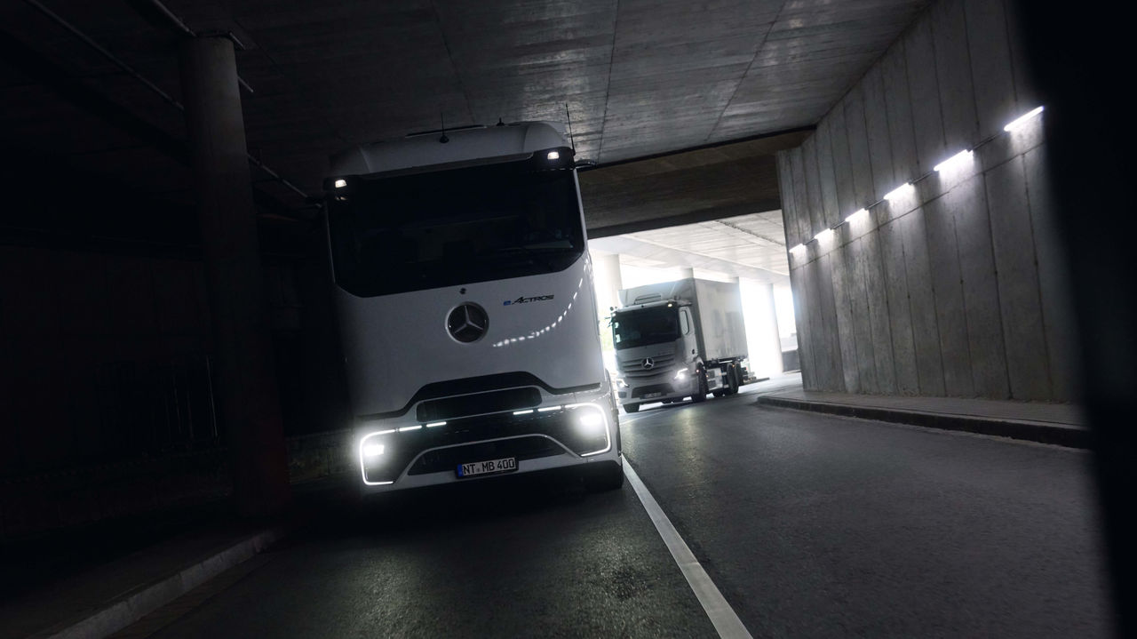 Twee eActros 400, een met de ProCabin en een met de vertrouwde cabine, rijden door een donkere tunnel met felle koplampen. Aan het einde van de tunnel is helder daglicht te zien, wat een contrast vormt met de donkere omgeving.
